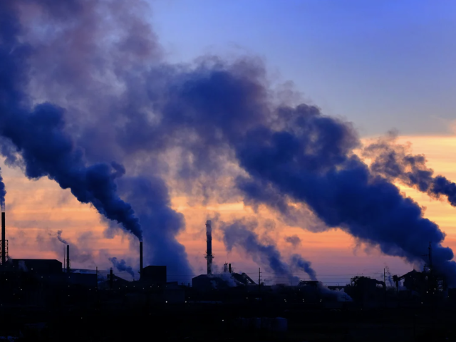 Smoke from factory stacks billows across the sky at dusk